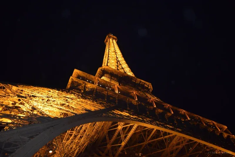The Eiffel Tower from directly beneath at night, its ironwork lit amber against a black sky.