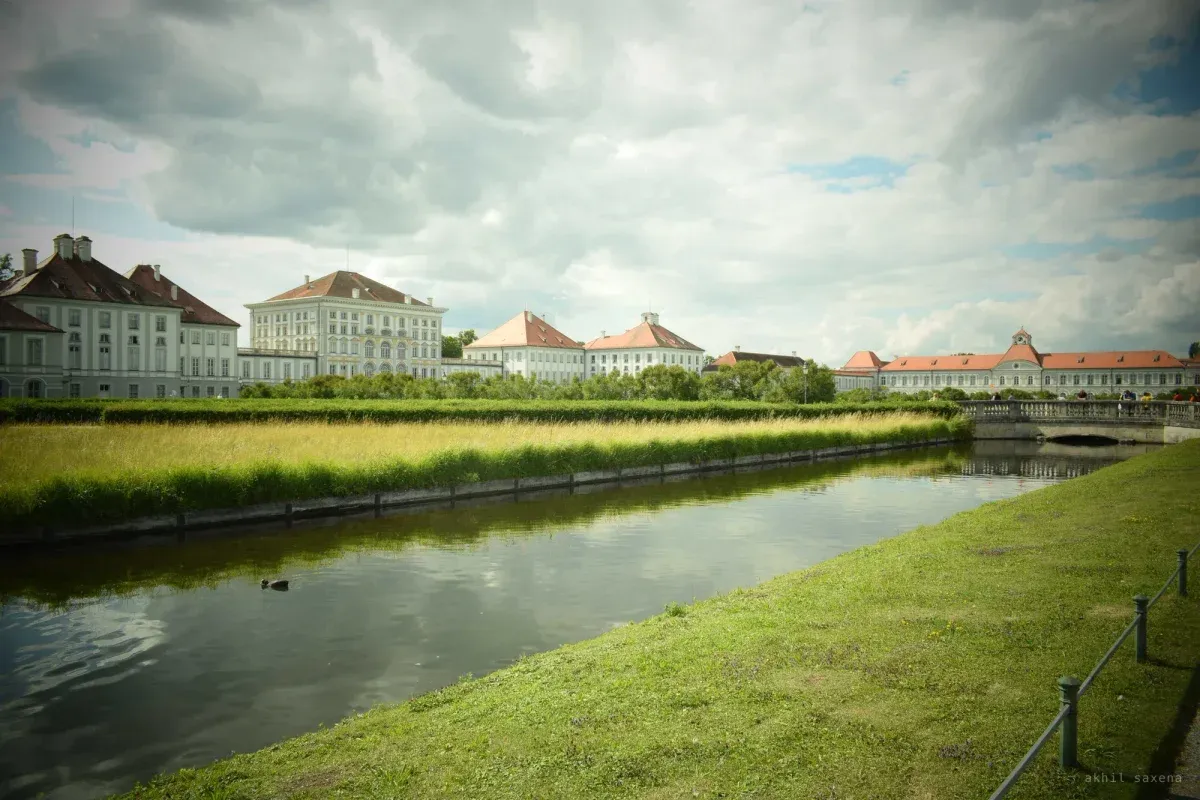 Nymphenburg's white baroque wings and red-tiled roofs stretched along a straight canal, reeds on the far bank under heavy cloud.