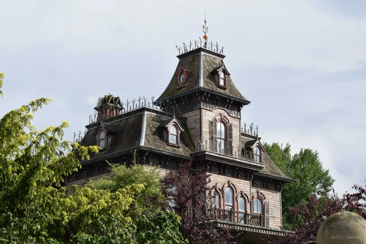 Phantom Manor's mansard roof, dormer windows and iron roof cresting, half screened by surrounding trees.