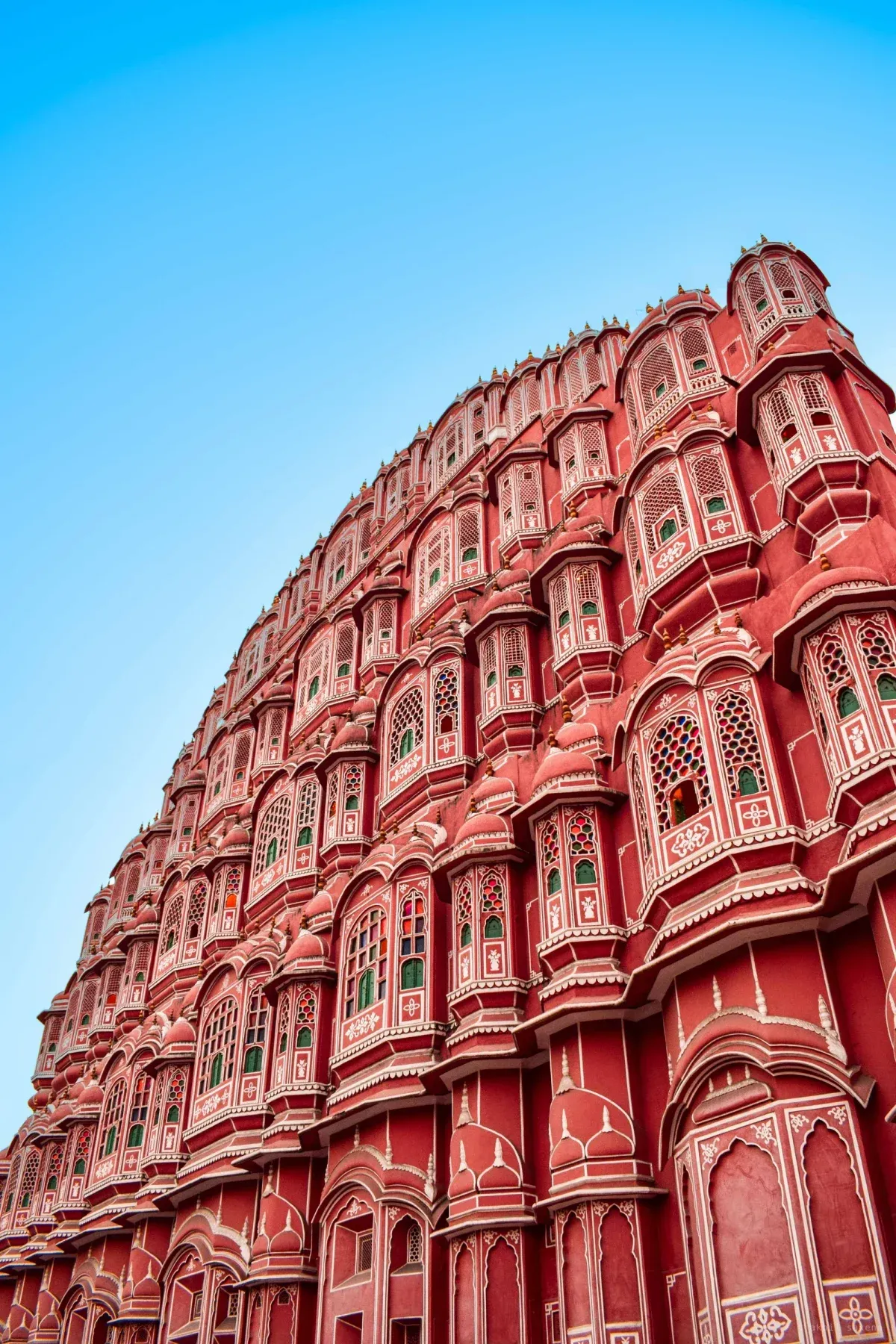 Hawa Mahal's five tiers of latticed windows rising in a curved pink sandstone facade, shot from the street against a clear sky.