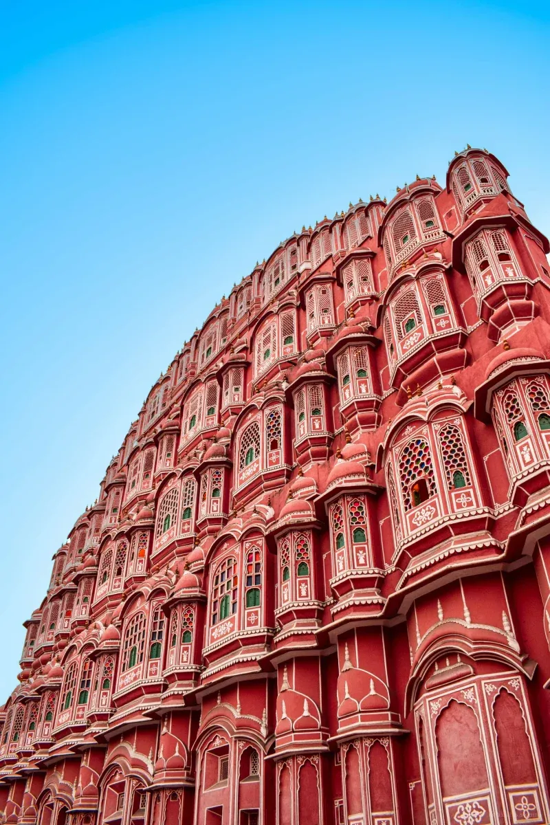 Hawa Mahal's five tiers of latticed windows rising in a curved pink sandstone facade, shot from the street against a clear sky.
