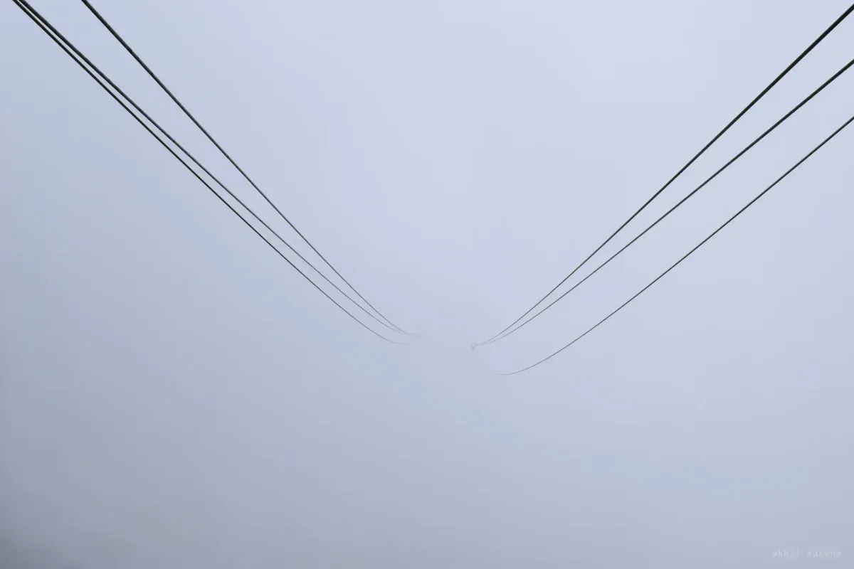 Two bundles of overhead cables descend from opposite corners and vanish into flat grey fog.