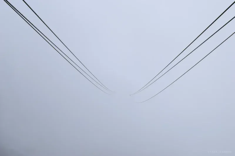 Two bundles of overhead cables descend from opposite corners and vanish into flat grey fog.