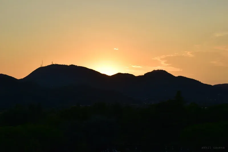 Two hill summits in silhouette against an orange sunrise, a communication mast on the left peak.